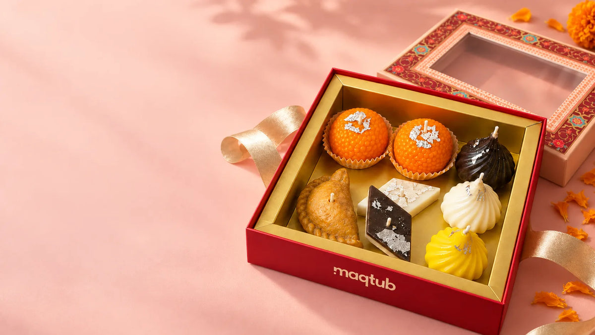 Maqtub mithai candle gift box with ladoo, modak, gujiya and kaju katli candles, a gold ribbon and marigolds