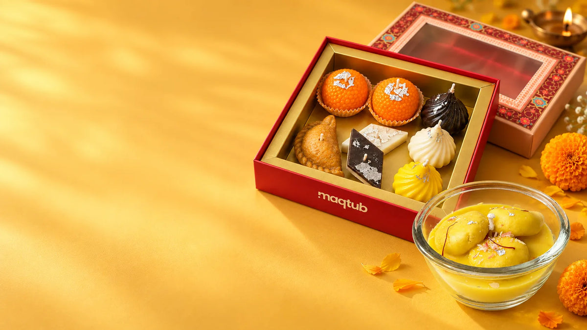 Maqtub mithai candle gift box with ladoo, modak, gujiya and kaju katli candles beside a bowl of rasmalai candles