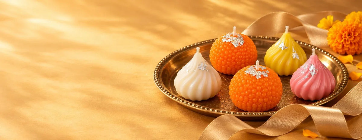Modak and motichur ladoo candles on a brass plate with gold ribbon and marigolds